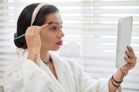 Téléchargez les photos : Femme regardant miroir et se brossant les sourcils - en image libre de droit