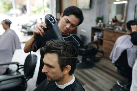 Téléchargez les photos : Coiffeur brushing cheveux fraîchement coupés du client - en image libre de droit