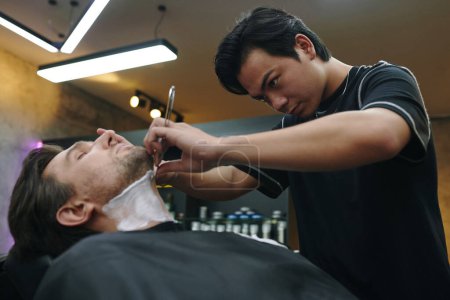 Téléchargez les photos : Concentré coiffeur cou de rasage du client avec rasoir pointu - en image libre de droit