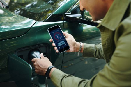 EV owner checking smart charger app on smartphone when plugging charging cable