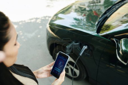 Electric car owner checking smart charger application on smartphone