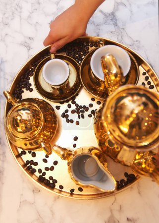 Photo for Golden tray with a golden teapot and gilded cups in the hands of a waiter - Royalty Free Image