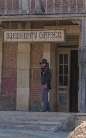Téléchargez les photos : Almeria Espagne - 09 15 2021 : Scènes de performance en direct, le shérif cow-boy regardant à l'extérieur de l'immeuble de bureaux du shérif, sur l'Oasys - Mini Hollywood, parc à thème espagnol occidental, désert d'Almeria Taberna - en image libre de droit