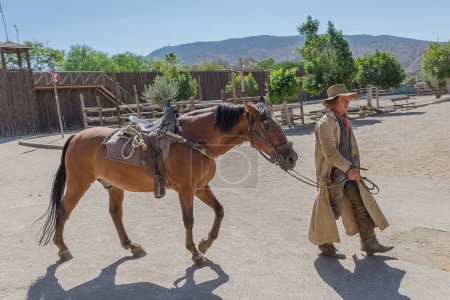 Téléchargez les photos : Almeria Espagne - 09 15 2021 : Vue de la performance en direct, cow-boy marchant avec son cheval, sur Oasys - Mini Hollywood, parc à thème espagnol occidental, scénario de cow-boys occidentaux, désert d'Almeria Taberna - en image libre de droit