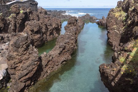 Téléchargez les photos : Île de Madère Portugal - 04 19 2023 : Vue des piscines naturelles sur le village de Porto Moniz, formé par des roches volcaniques, îlot de taupe en arrière-plan, côte de l'île de Madère, Portugal - en image libre de droit