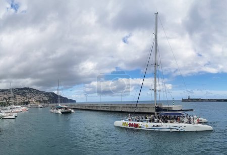 Foto de Isla de Madeira Portugal - 04 19 2023: Vista de Catamaranes llenos de turistas, regresando de un tour de observación de delfines, ballenas y tortugas, frente a la costa de Funchal, isla de Madeira - Imagen libre de derechos