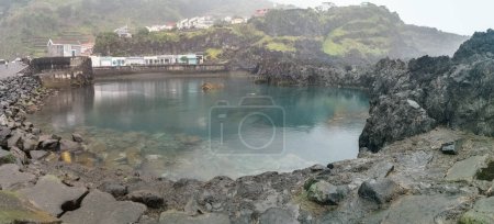 Foto de Isla de Madeira Portugal - 04 19 2023: Vista de las piscinas naturales en el pueblo de Seixal, formado por rocas volcánicas, pueblo como fondo, costa de la isla de Madeira, Portugal - Imagen libre de derechos