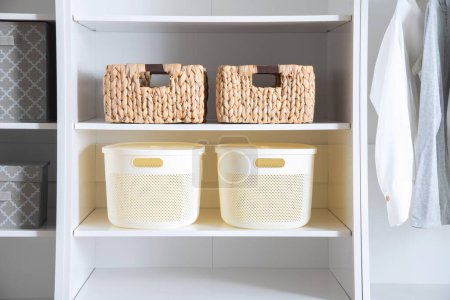 Esta imagen representa un armario blanco con múltiples cestas en los estantes y varios artículos de ropa colgando de la barra del armario