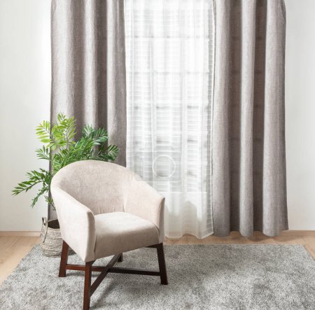 a white modern armchair situated near a window, with a light-colored curtain inside an empty lounge