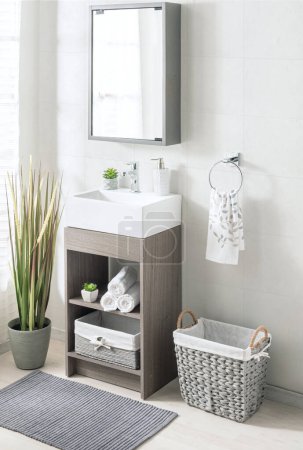 Modern Scandinavian-style bathroom interior with a white bathtub, ceramic bathroom vessel vanity, and gray wicker basket