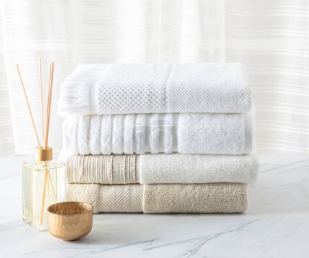 Weiße Baumwollhandtücher gefaltet und Aromadiffusor auf einem Tisch aus weißem Marmor im Badezimmer. Neutrale Farbe, Nahaufnahme
