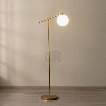 Photo for An illuminated golden floor lamp in an empty room, casting a warm, inviting glow throughout the space - Royalty Free Image