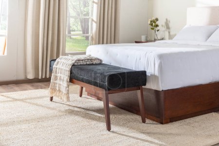 Téléchargez les photos : Une chambre à coucher avec un couvre-lit blanc et un banc en bois, espace intérieur confortable chambre à coucher, gros plan - en image libre de droit