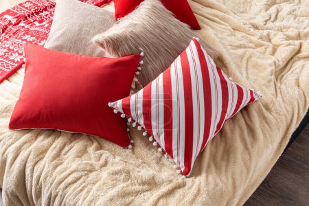 Foto de Almohadas y cojines de Navidad rojos y blancos en la cama con una manta beige claro extra suave, primer plano. Diseño de interiores - Imagen libre de derechos