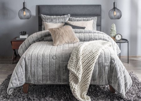 Cama gris con mantas y almohadas a cuadros de punto en un moderno interior de dormitorio nórdico