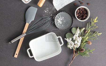 Flat lay composition of kitchen silicone utensils, baking set, and Christmas branches evergreens on a grey background, top-view
