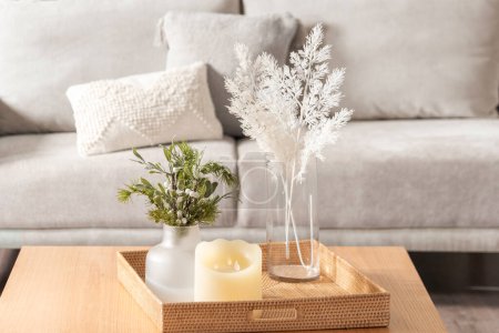 Téléchargez les photos : Vase avec des fleurs et des bougies dans un plateau en rotin sur une table en bois dans un salon moderne, décoration intérieure scandinave, fond de loveseat - en image libre de droit