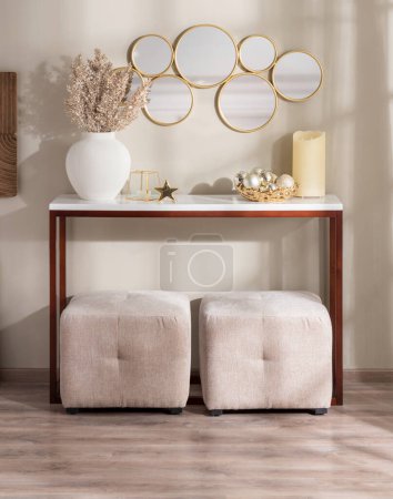 Cozy living room interior featuring a wooden console table with household ornaments and beige cube ottomans, a hanging mirror on a beige wall