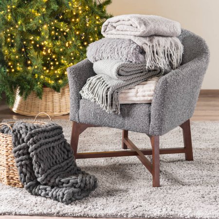 Cozy Nordic Winter Living Room with Grey Armchair, Warm Folded Blankets, Knitted Plaids, Illuminated Christmas Tree, All in Natural Light & Neutral Colors
