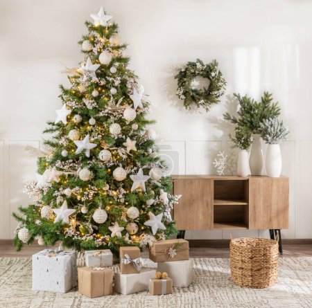 Foto de Salón de Navidad, con un árbol de Navidad artificial adornado con esferas blancas y estrellas, junto con guirnaldas y cajas de regalo, junto a una Credenza de madera, luz natural - Imagen libre de derechos