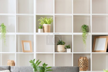 Foto de Moderno diseño interior minimalista de la sala de estar con una librería de espacios cuadrados blancos, un sofá gris y plantas, cuidadosamente organizadas para un ambiente hogareño, iluminadas por la luz natural. - Imagen libre de derechos