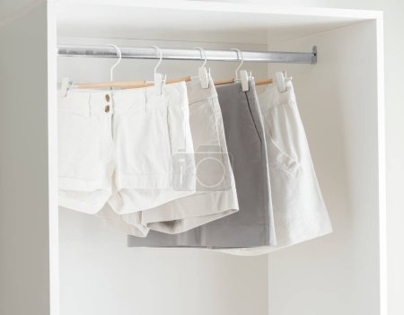 Photo for Bright White Room with White and Gray Pleated Women Shorts Hanging on a Clothes Rail, Displayed in a White Wardrobe with a Plain Pants Hanger - Royalty Free Image
