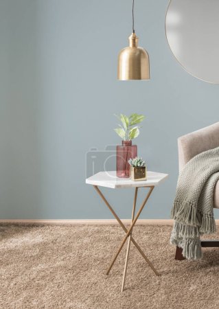 Photo for Interior of a Modern Living Room with White Marble Accent Table Featuring a Gold Finish Base Adorned with a Flower Arrangement in Glass Vases and Armchair with a Throw Blanket, Gray Walls. - Royalty Free Image