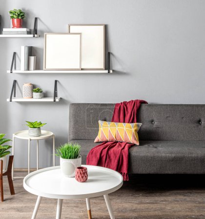 Photo for Living Room Interior Featuring Grey Armless Sofa, White Round Coffee Table with Wooden Legs, and White Floating Shelves with Decorative Potted Plants and Two Vertical Wooden Blank Frame Mock-Ups. - Royalty Free Image