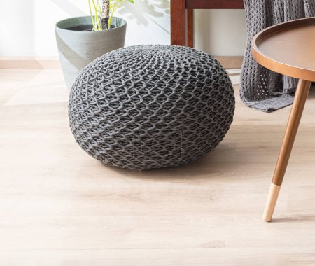Photo for Grey Modern Knitted Fabric Cotton Round Pouf Next to a Decorative Round Side Table on a Wooden Floor in a Bright Living Room. - Royalty Free Image