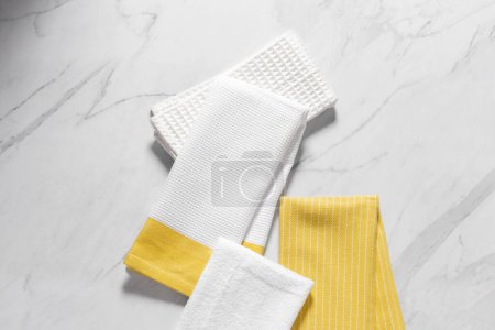 Téléchargez les photos : Ensemble de serviettes de cuisine en coton multicolore jaune et blanc, décorativement plié et empilé l'un sur l'autre sur un fond de table en marbre blanc, vue sur le dessus. - en image libre de droit