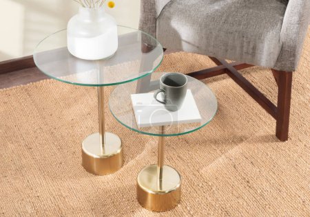 Photo for Coffee Cup and Decorative Glass Table Vase on Round Brass Glass Top Accent Table, Beside a Grey Fabric Lounge Chair in a Modern Living Room, Interior Design Concept, with an Area Rug, Top View. - Royalty Free Image