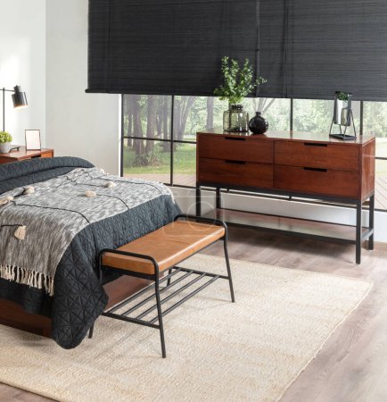 Mid-Century Modern Bedroom: Charcoal Quilted Bedspread on Cozy Bed, Sleek Walnut Wood Sideboard with Decorative Green Plant, Brown Leather Bench on Black Metal Frame, Set Against a Bright Window.