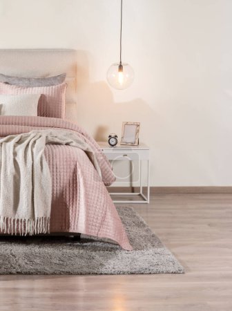 Ruhige Schlafzimmer-Essenz mit weichem rosa gesteppten Bettdecke auf gemütlichem Bett, Drapieren Neutral-Farbton Throw, grauer Teppich unten, modernes Globenlicht beleuchtet weißen Nachttisch, warme Holzböden.