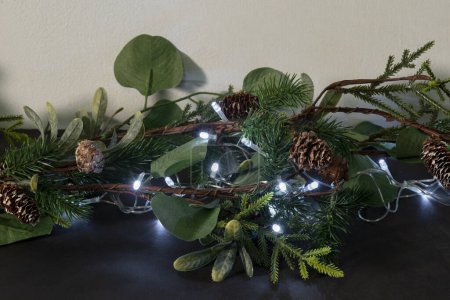 Photo for Christmas Garland Decoration, Lush Greenery, Pinecones, and Silver LED Lights on Dark Surface, Twinkling Amidst Eucalyptus Leaves and Spruce Twigs, Festive Holiday Ornament for Home Interiors. - Royalty Free Image