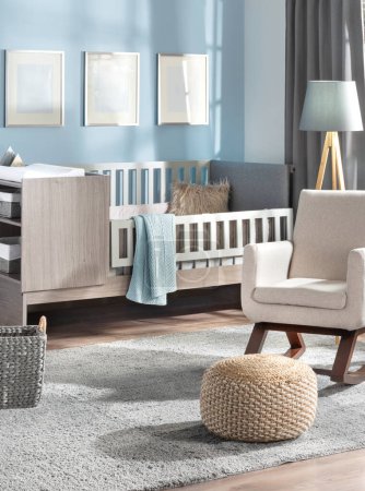 Photo for Contemporary baby's room with pastel blue walls, showcasing a gallery mockup of three blank frames, a sleek wooden crib featuring a grey cushion, an adjacent beige armchair, and a plush grey area rug. - Royalty Free Image