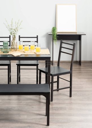 Téléchargez les photos : Sunny Morning Breakfast Nook Doté d'un ensemble de salle à manger noire avec chaises et banc, jus d'orange rafraîchissant sur la table, un cadre photo blanc sans ornement et des plantes vert vif éclaircissant l'espace. - en image libre de droit