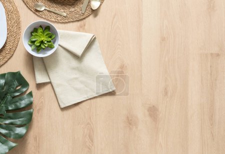 Draufsicht auf eine Küche flach gelegt, Holzoberfläche mit Kopierraum, erdige Texturen, Faser-Tischset, Leinen-Serviette, Porzellanschale, eine grüne Sukkulente, Monstera Blatt, Utensilien, Bio-Wohnkonzept.