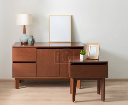 Mid-Century Modern Interior Design: Rich Wooden Sideboard with Tapered Legs, Accompanied by a Matching Nightstand, Adorned with a Vintage Lamp, Decorative Vases, and a Frame Mock-up Artistic Display.