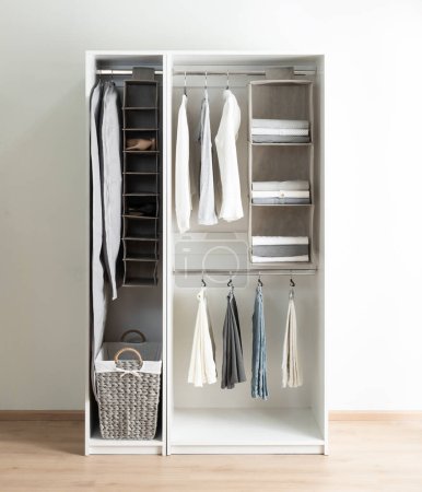 White Wardrobe, Gray Hanger Closet Storage Set, Folded Linens, Woven Laundry Basket, and Neatly Organized Clothes on Hangers in a Tranquil Bedroom, Efficient Interior Design, Tidy Apparel Keeping.