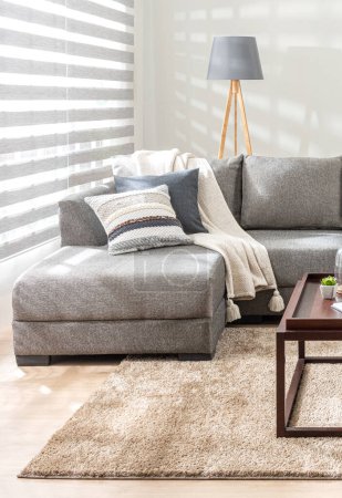 Sala de estar escandinava inspirada en el otoño con luz natural que ilumina una acogedora sección en tela texturizada, almohadas de punto y tiro de borla, una lámpara de piso de trípode de madera y alfombra beige de felpa.