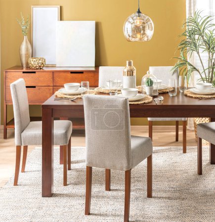 Einladender Speisesaal mit einem reichhaltigen Holztisch mit passenden Stühlen, die mit neutralem Stoff gepolstert sind und auf einem strukturierten Webteppich liegen. Ein Beistelltisch, moderne Accessoires, warme senffarbene Wand, Grün