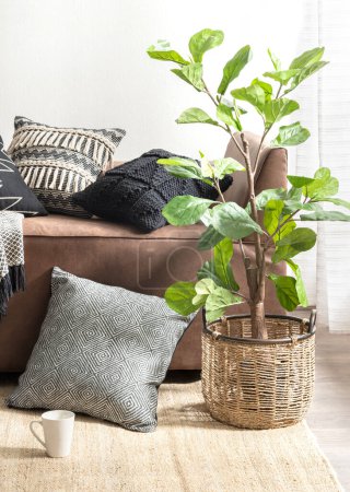 Coin salon accueillant avec un canapé en daim, un assortiment de coussins tricotés aux motifs et textures variés, une jardinière à panier tissée avec une plante ornementale, posée sur un tapis en fibre, lumière du jour.