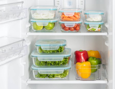 Estantes de refrigerador organizados eficientemente con variedad de productos frescos en recipientes transparentes, destacando el almacenamiento de alimentos limpios y una vida saludable en un entorno de cocina moderno.