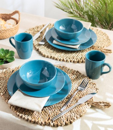 Coastal-Inspired Dining Setting with Vibrant Teal Dinnerware Set upon Woven Seagrass Placemats, Silver Flatware and Linen Napkins, on a Light Wood Table with a Lush Green Plant Accent, Fresh vibes.