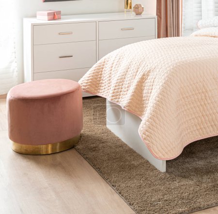 Elegante interior femenino dormitorio en suaves tonos rosados con lujosas camas, un otomano de terciopelo redondo con base dorada, un Dresser minimalista blanco, Textiles coordinados, haciendo hincapié en la comodidad y el estilo.
