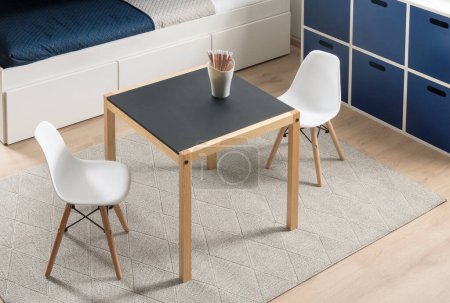 Kinderzimmer im skandinavischen Stil mit minimalistischem Tafel-Tisch und ikonischen weißen Schalenstühlen, hölzernen Aufbewahrungswürfeln und neutral gewebtem Teppich, kreativen Spiel- und Lernaktivitäten.