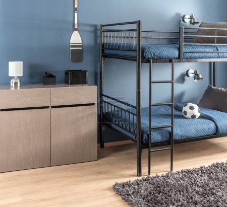Modernes Jungenzimmer mit robustem schwarzem Metall-Etagenbett, aufeinander abgestimmten marineblauen Bettdecken, schlankem grauen Aufbewahrungsschrank, Wandlampen im industriellen Stil, Plüsch-grauem Shag-Teppich und einem klassischen Fußballakzent.