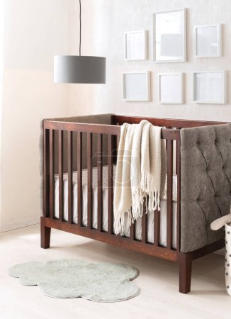 Tranquille chambre de bébé avec un lit d'enfant traditionnel en acajou avec un jet de crème douce, une chaise arrière grise touffetée et un tapis vert pâle en forme de nuage capricieux. Cadres photo vides blancs ornent le mur.