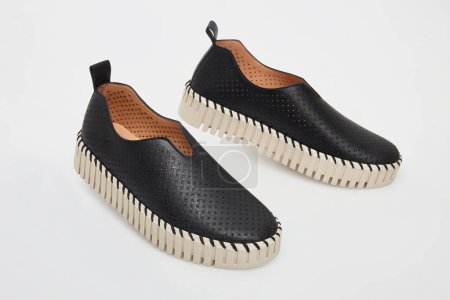 Stylish black casual slip-on shoes for everyday wear, a perforated leather design for enhanced breathability, complemented by a distinctive cream serrated rubber sole for optimal comfort and elegance.
