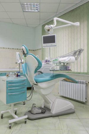 Un cabinet dentaire moderne dispose d'une chaise dentaire élégante bleue et blanche. Le cadre métallique brille sous les plafonniers, créant une atmosphère propre et professionnelle.